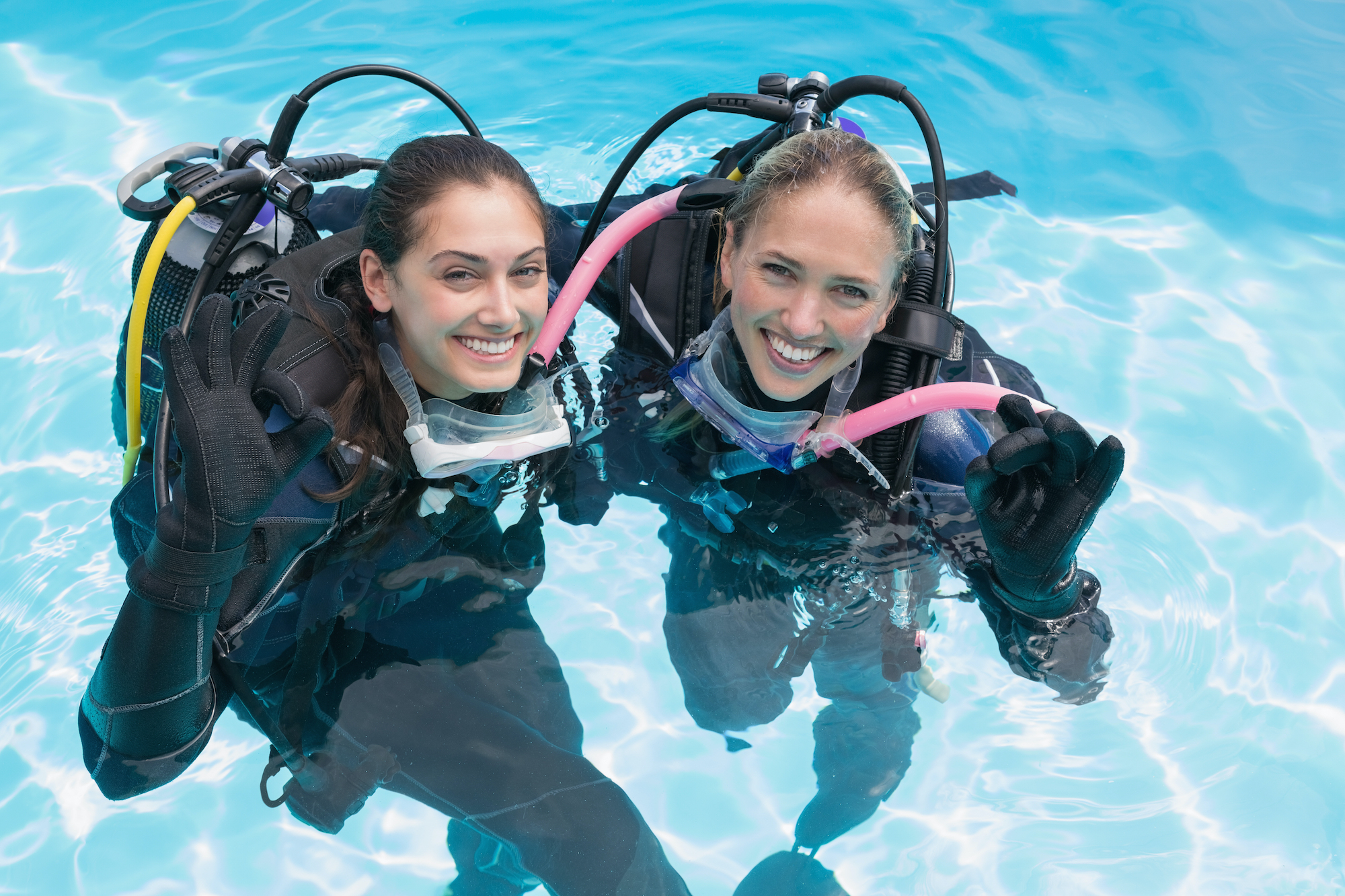 Amigos sonrientes en entrenamiento de buceo en piscina haciendo señal de ok en un día soleado