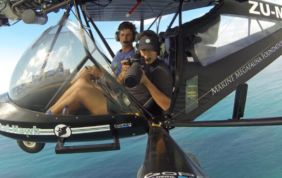 a marine scientist in a helicopter over the ocean holding a camera