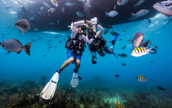 divers underwater in Belize make a heart shape with their arms